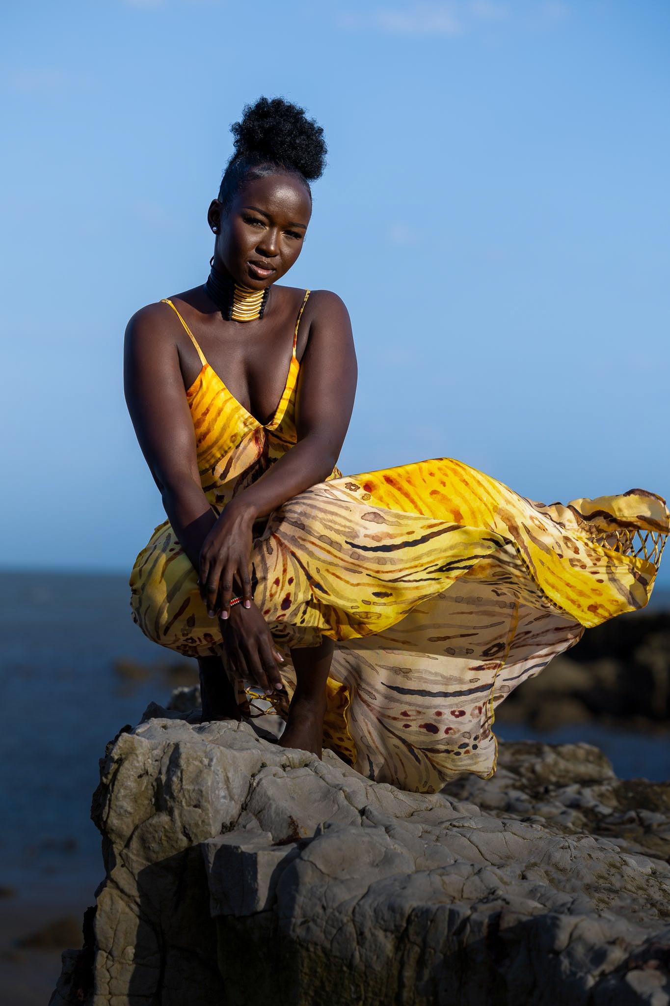 Woman in a yellow dress sitting on a rock by the ocean